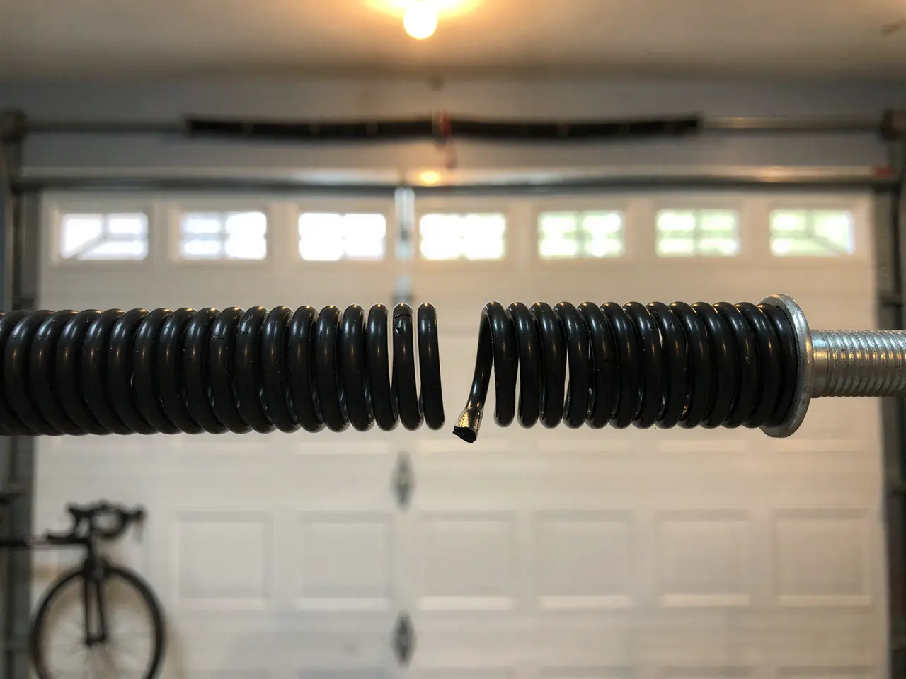 A broken black torsion spring is visible in front of a white garage door.